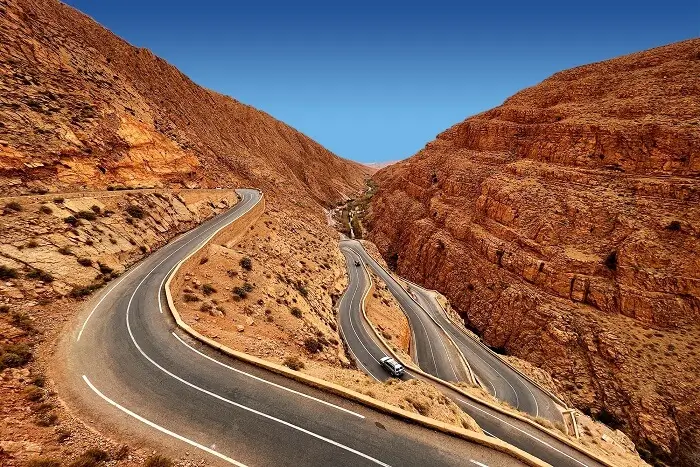 Mountain road with hairpin turns and two vehicles Winding mountain road with sharp turns through dry rocky terrain under clear blue sky.