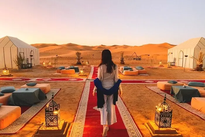 Desert camp walkway at sunset with lanterns and tents Person walking on red carpet between cushions and lanterns in a desert camp at sunset