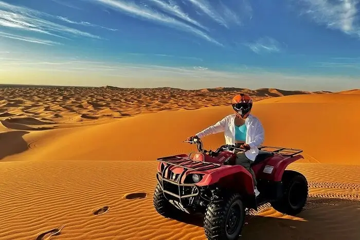 Rider on Red ATV in Desert Sand Dunes Person wearing helmet and jacket riding red ATV on sand dunes under blue sky with clouds