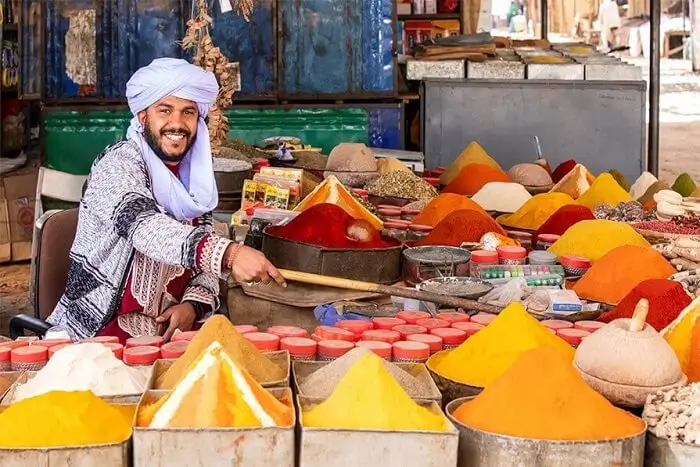 Market vendor presenting colorful spices at stall Man in a light blue turban selling colorful spices in conical piles at a market stall