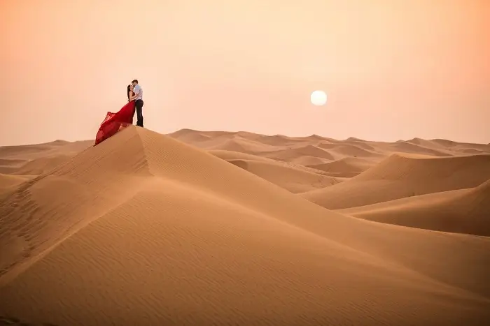 Romantic couple embracing on the golden Sahara dunes of Erg Chebbi near Merzouga at sunset during their Morocco honeymoon