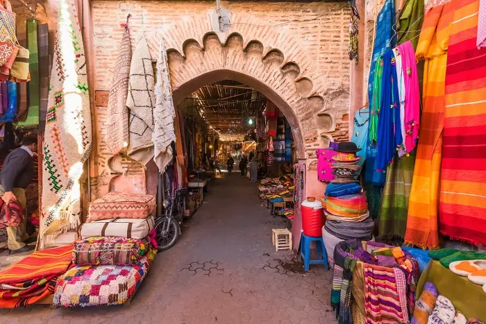 Traditional archway leading into the Marrakech Medina souk with colorful rugs and market stalls on a Morocco 15 Day Tour from Casablanca