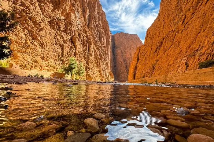 The stunning red rock cliffs and crystal clear river of the dramatic Todgha Gorges near Tinghir on a Morocco 2 week itinerary