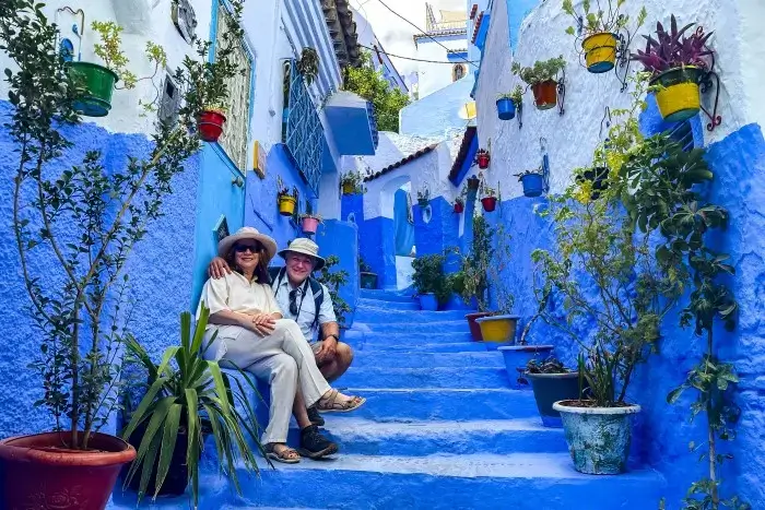 A tourist couple sitting on the blue painted steps of a charming alleyway in the Blue City of Chefchaouen on a two week Morocco itinerary